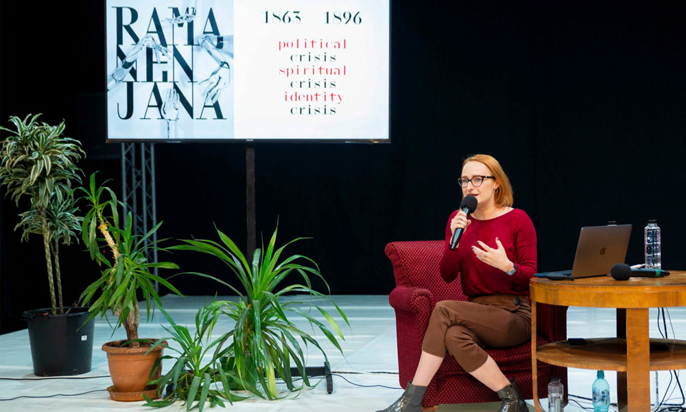 Simona Deaconescu sitting on stage with mic in hand.