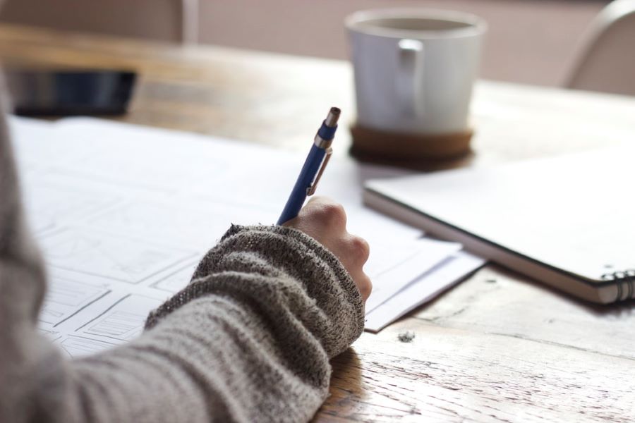 Forearm writing on papers with cup of coffee