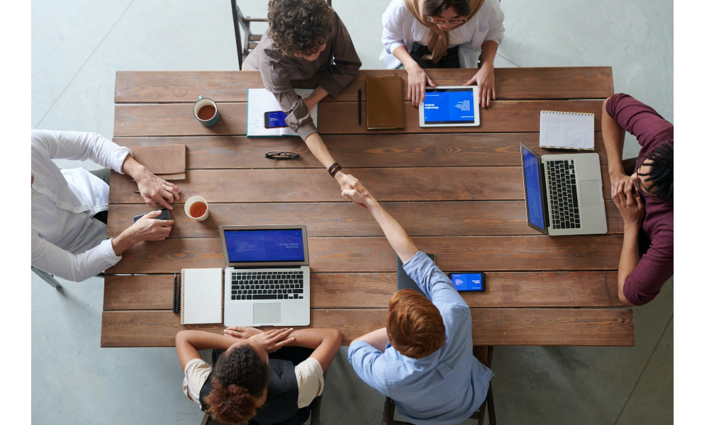 Individuals sitting around a large table working on laptops