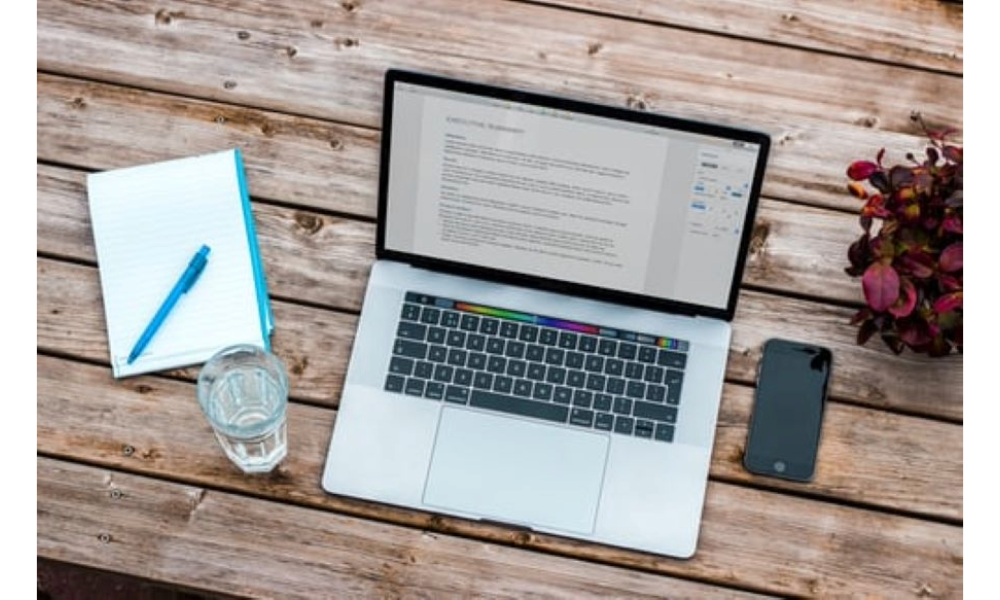 laptop sitting open alongside pen, paper and a glass of water.