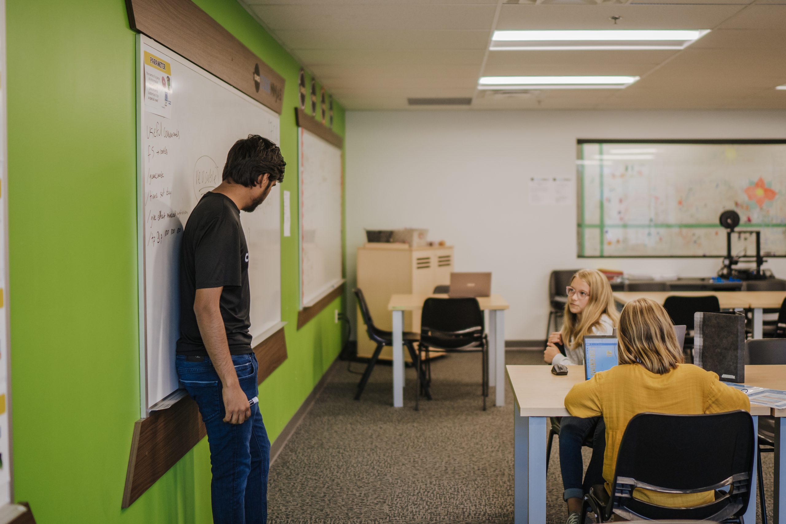 Co-op Student presenting information from a whiteboard to two kids seated at a desk.