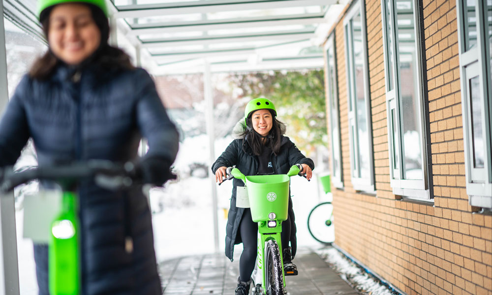 Two people riding e-bikes on campus