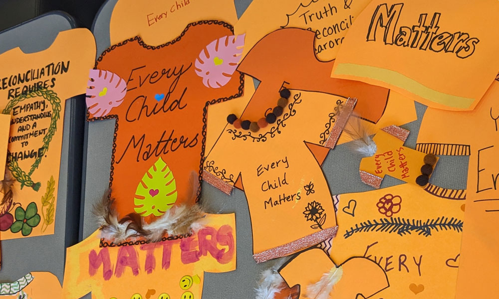 Paper cut outs of orange paper shirts with Every Child Matters written on them.