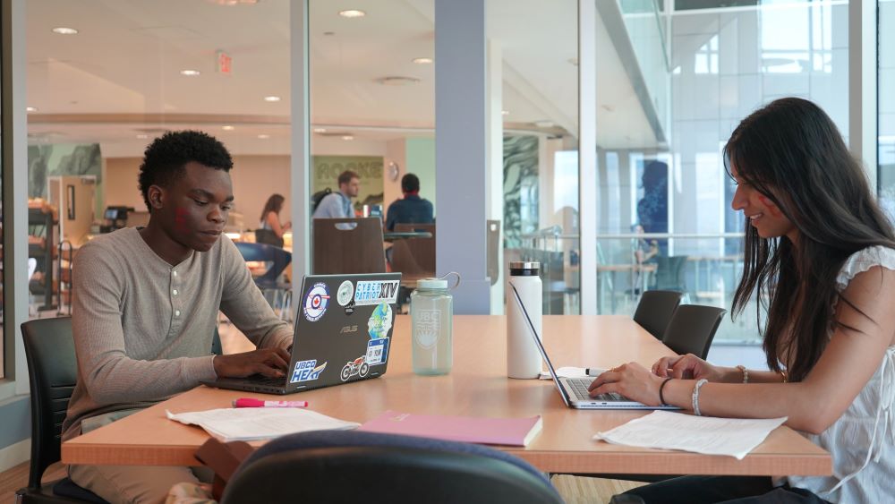 Two UBC Okanagan Engineering students sit at a table working on laptops in a study room on campus.