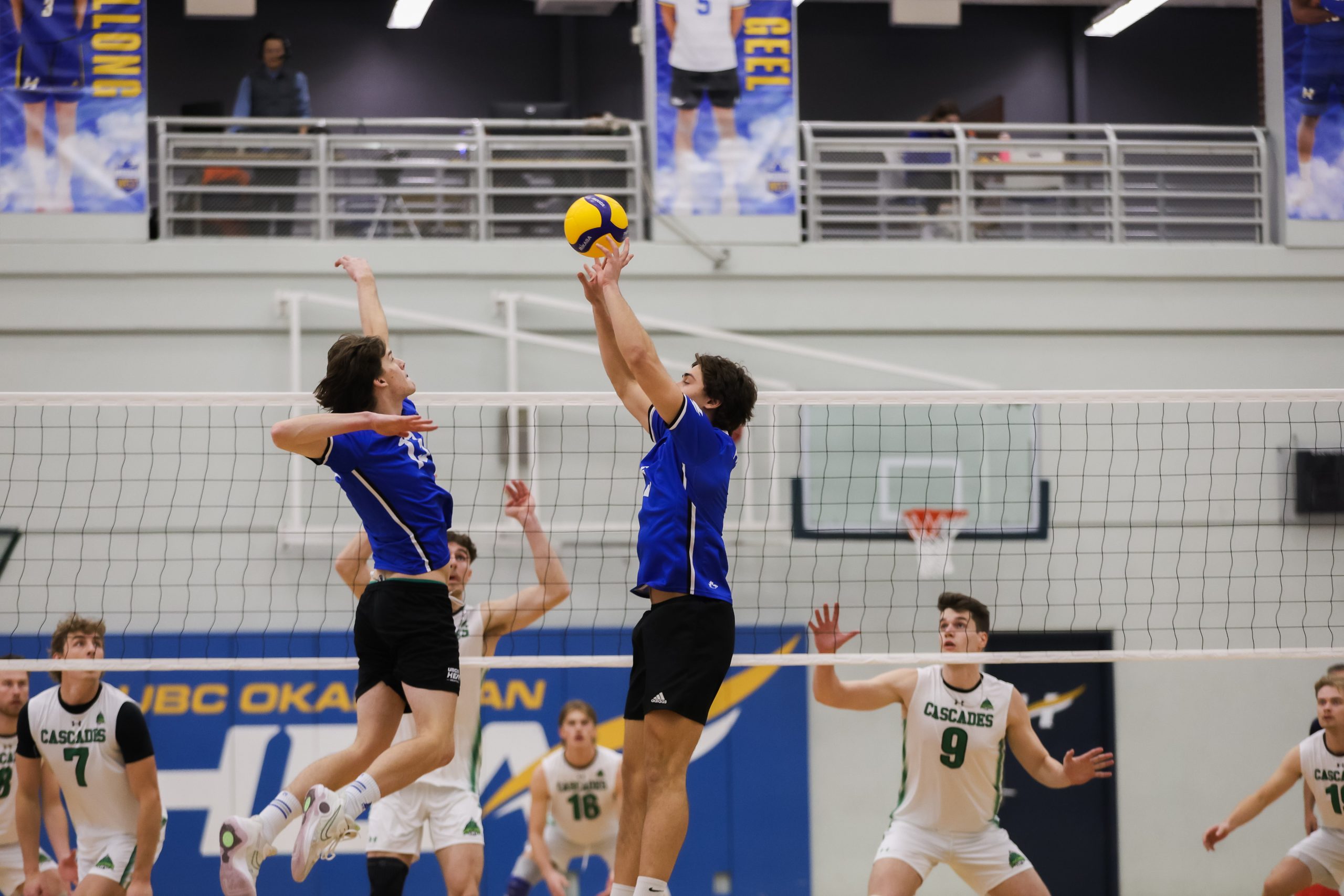 Two volleyball players jumping to spike a ball